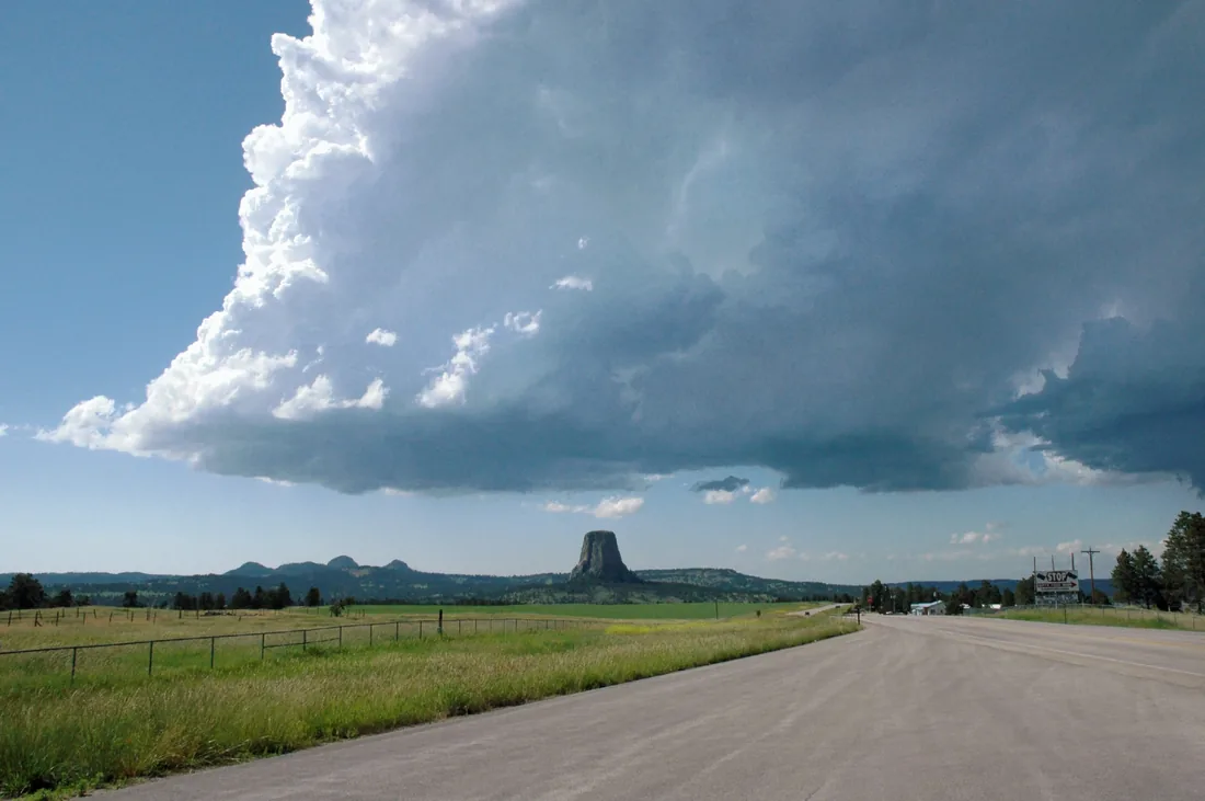 Devils Tower standing beneath a towering thunderhead, seen from Wyoming Highway 24.